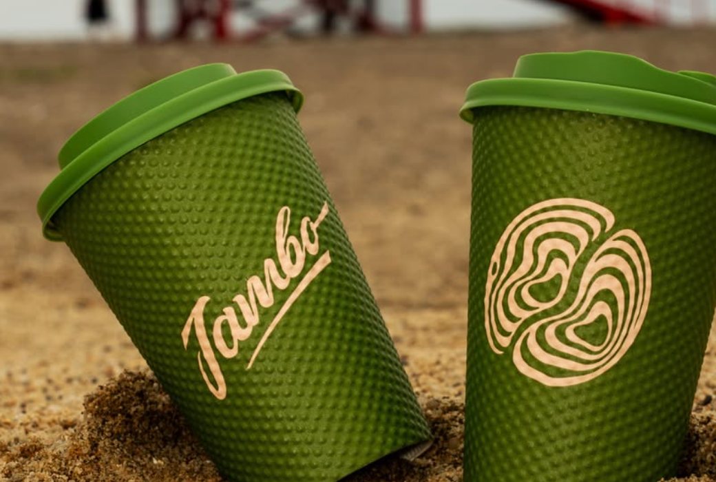 Two green dotted Jambo cups standing in sand, one with the script logo and one with the swirl emblem